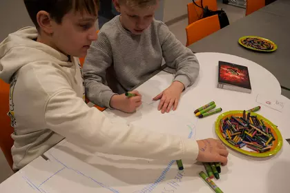 Dzieci rysują kredkami przy stole podczas warsztatów plastycznych.