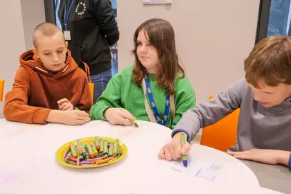 Troje dzieci rysuje przy okrągłym stole podczas warsztatów.