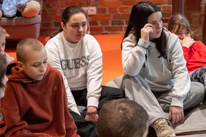 Dzieci siedzą w kręgu i słuchają prowadzącej warsztaty.