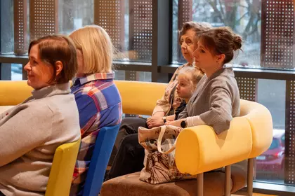 Babcie i dziadkowie z wnukami siedzą na widowni podczas spotkania w bibliotece.