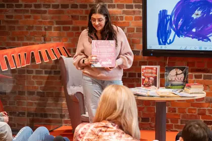 Prowadząca prezentuje książkę dzieciom podczas spotkania międzypokoleniowego.