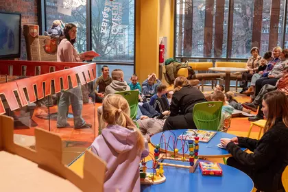 Rodzinne spotkanie w bibliotece, dzieci i dorośli słuchają czytania.