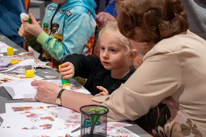 Dziecko z babcią pracują przy stoliku podczas zajęć plastycznych.