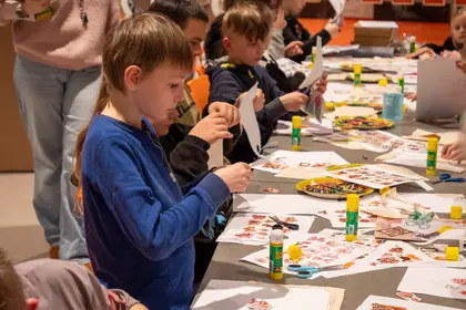 Dzieci wykonują prace plastyczne przy długim stole w bibliotece.