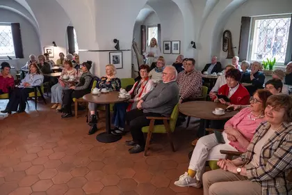 Publiczność siedzi przy stolikach podczas wydarzenia w bibliotece.