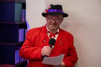 Mężczyzna w czerwonej marynarce mówi do mikrofonu.