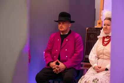Mężczyzna w kapeluszu siedzi obok kobiety w ludowym stroju.