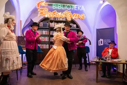 Tancerze występują przed publicznością w bibliotecznej sali koncertowej.