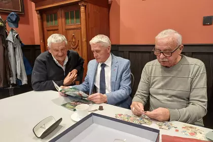 Trzech mężczyzn ogląda eksponaty filatelistyczne przy stole.