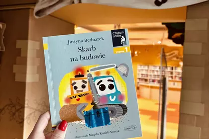 Książka „Skarb na budowie” trzymana przed wejściem do biblioteki dziecięcej.