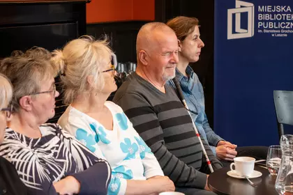 Grupa uczestników siedzi podczas rozmowy prowadzonej w bibliotece.