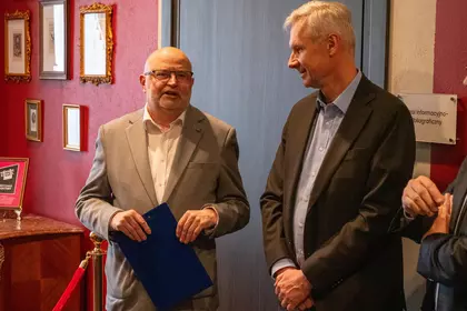 Dwóch mężczyzn rozmawia podczas uroczystości w zabytkowym gabinecie.