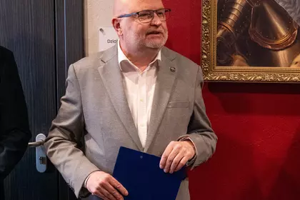 Mężczyzna w jasnej marynarce trzyma dokument i przemawia.