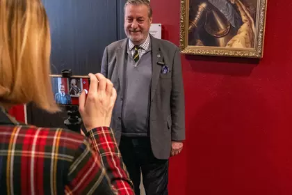 Kobieta robi zdjęcie mężczyźnie stojącemu przy czerwonej ścianie.