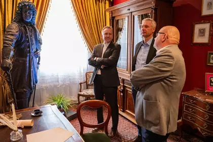 Mężczyźni rozmawiają w gabinecie z zabytkowymi meblami i rzeźbą.