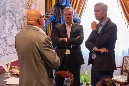Trzech mężczyzn prowadzi rozmowę w historycznym wnętrzu.
