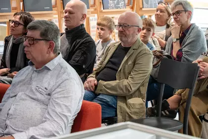 Publiczność siedzi w rzędach i słucha wydarzenia.