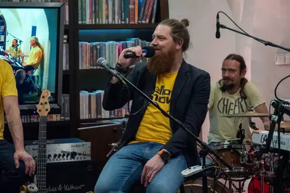 Prowadzący rozmawia z muzykami na scenie.