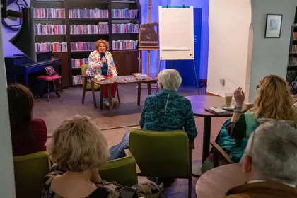 Autorka prowadzi spotkanie autorskie w Bibliotece Ratuszowej, siedząc przed publicznością na tle reg