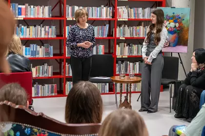 Prowadząca i młoda artystka podczas spotkania autorskiego w bibliotece wśród publiczności.
