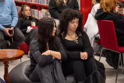 Dwie uczestniczki siedzą na pufie podczas wydarzenia literacko-artystycznego w bibliotece.