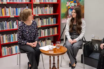 Rozmowa podczas wydarzenia literackiego przy stoliku na tle bibliotecznych regałów.