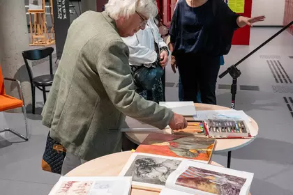 Uczestnicy wydarzenia oglądający szkicowniki, albumy i pastele przygotowane przez artystkę.