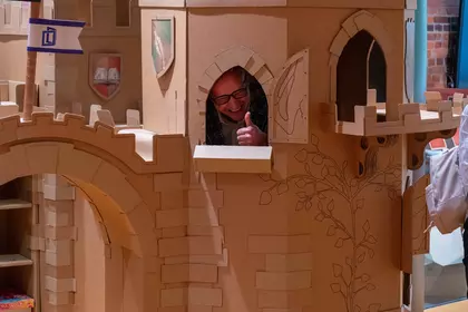 Mężczyzna zagląda przez okno kartonowego zamku w strefie dziecięcej.