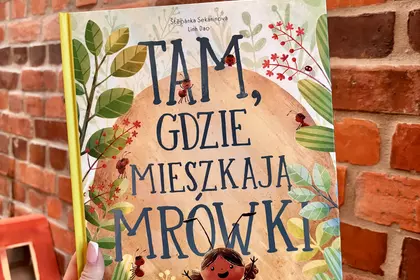 Książka „Tam, gdzie mieszkają mrówki” trzymana przy ceglanej ścianie