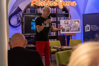 Prelegent prowadzi spotkanie o jazzie pod neonem Biblioteki Ratuszowej.