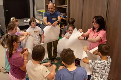 Dzieci i prowadzący wykonują ćwiczenia z wykorzystaniem kartek papieru.
