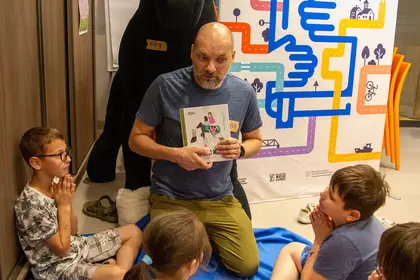 Prowadzący czyta dzieciom książkę podczas bibliotecznego spotkania.