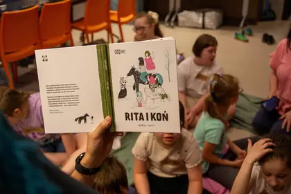 Prowadzący prezentuje dzieciom książkę „Rita i Koń”.