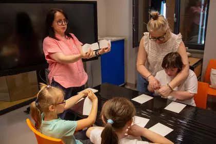 Dzieci wykonują zadania plastyczne przy stole warsztatowym.