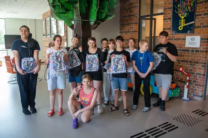 Starsi uczestnicy prezentują pamiątkowe plecaki po warsztatach.