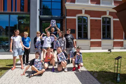 Uczestnicy pozują z plecakami przed budynkiem biblioteki.