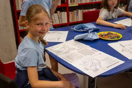 Dziewczynka wykonuje zadanie przy stole z materiałami edukacyjnymi.