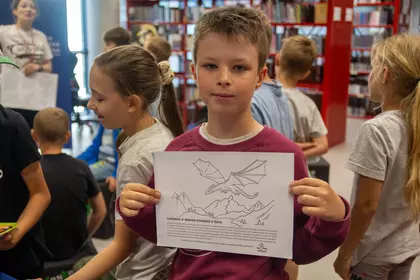 Chłopiec prezentuje wykonaną kartę pracy z ilustracją smoka.
