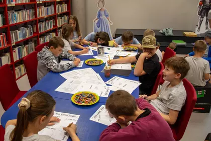 Uczestnicy zajęć siedzą razem w bibliotecznej przestrzeni.