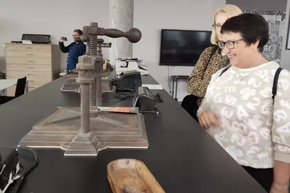 Uczestniczki wizyty oglądają zabytkową prasę drukarską w bibliotece.