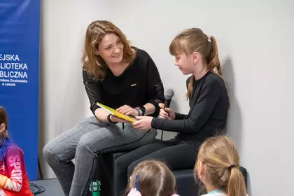 Uczestniczka czyta fragment książki podczas spotkania w bibliotece.