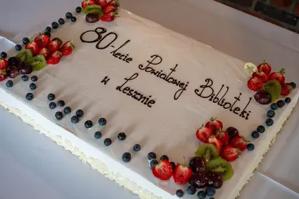 Tort z napisem „80-lecie Powiatowej Biblioteki w Lesznie” udekorowany owocami.