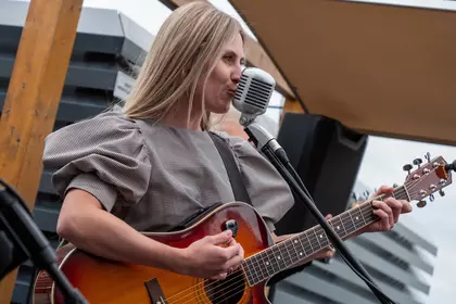 Wokalistka śpiewa i gra na gitarze akustycznej podczas koncertu.