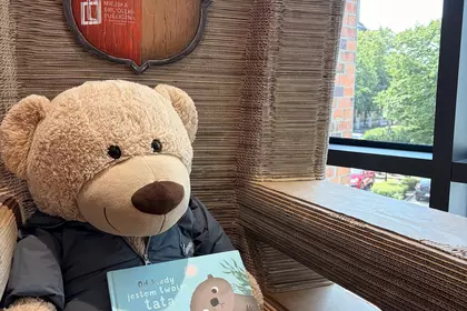 Pluszowy miś siedzi w bibliotecznym fotelu i trzyma książkę „Od kiedy jestem twoim tatą”.