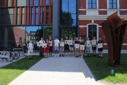 Dwóch uczestników warsztatów maluje materiałowe torby przy wspólnym stole.