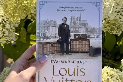 Dłoń trzyma książkę „Louis Vuitton. Opowieść o wielkim marzeniu” na tle hortensji.