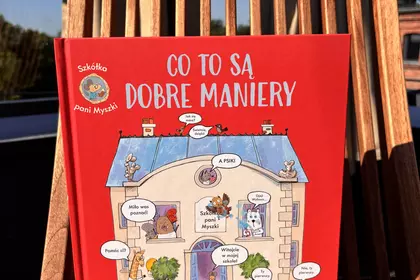 Książka „Co to są dobre maniery” Jamesa Maclaine’a ustawiona na drewnianym krześle w promieniach sło