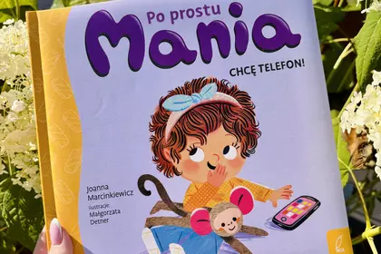 Książka „Po prostu Mania. Chcę telefon!” trzymana na tle kwitnących hortensji.
