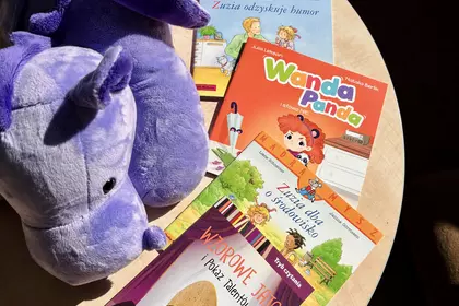 Pluszowy hipopotam przygląda się książkom dla dzieci rozłożonym na stoliku w bibliotece.