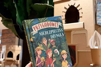 Książka „Przygodowcy. Niebezpieczna dżungla” na tle dziecięcego zamku i drzewa.